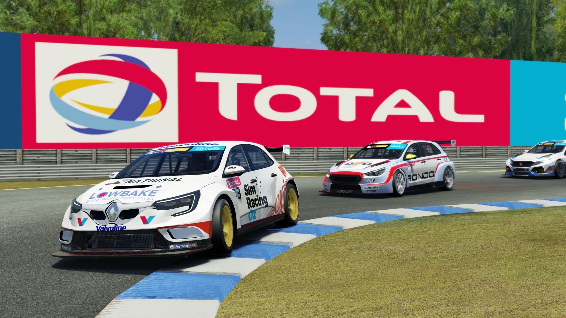 Sim racing screenshot of the white Lowbake Renault Megane TCR car cornering in front of a giant Total sign, with other cars behind