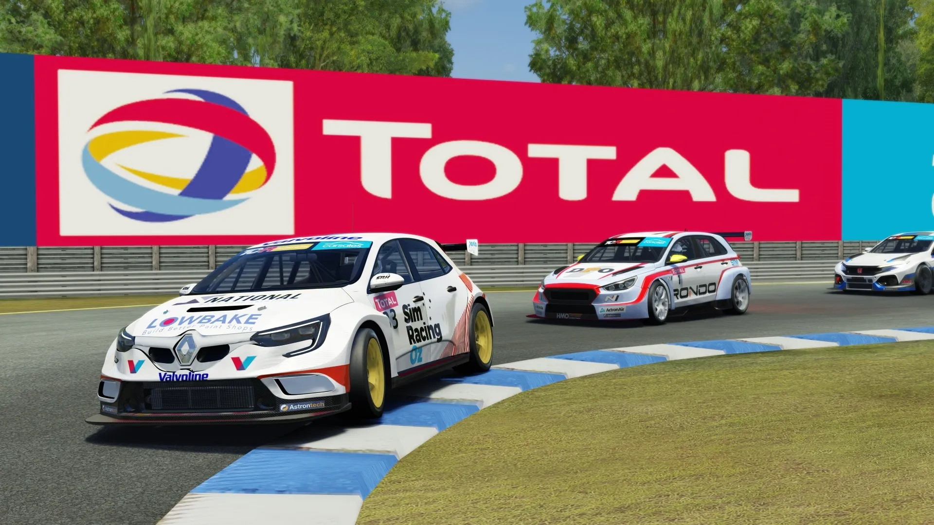 Sim racing screenshot of the white Lowbake Renault Megane TCR car cornering in front of a giant Total sign, with other cars behind