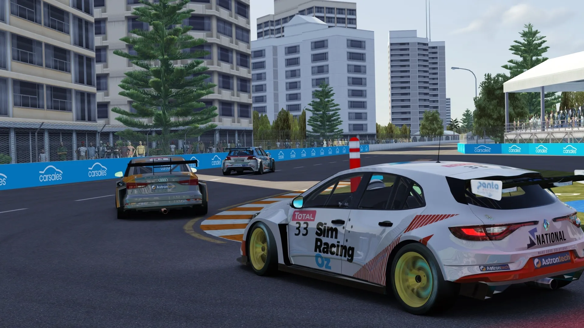 Sim racing screenshot of the white #33 Sim Racing Oz Renault TCR car from behind on a street circuit with Carsales signs