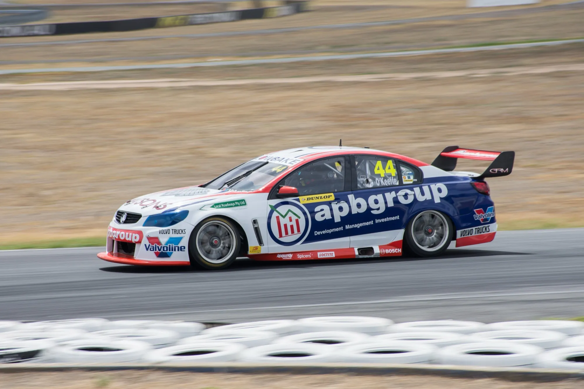 The #44 apbgroup Commodore Supercar in profile on track beside a wall of stacked tyres