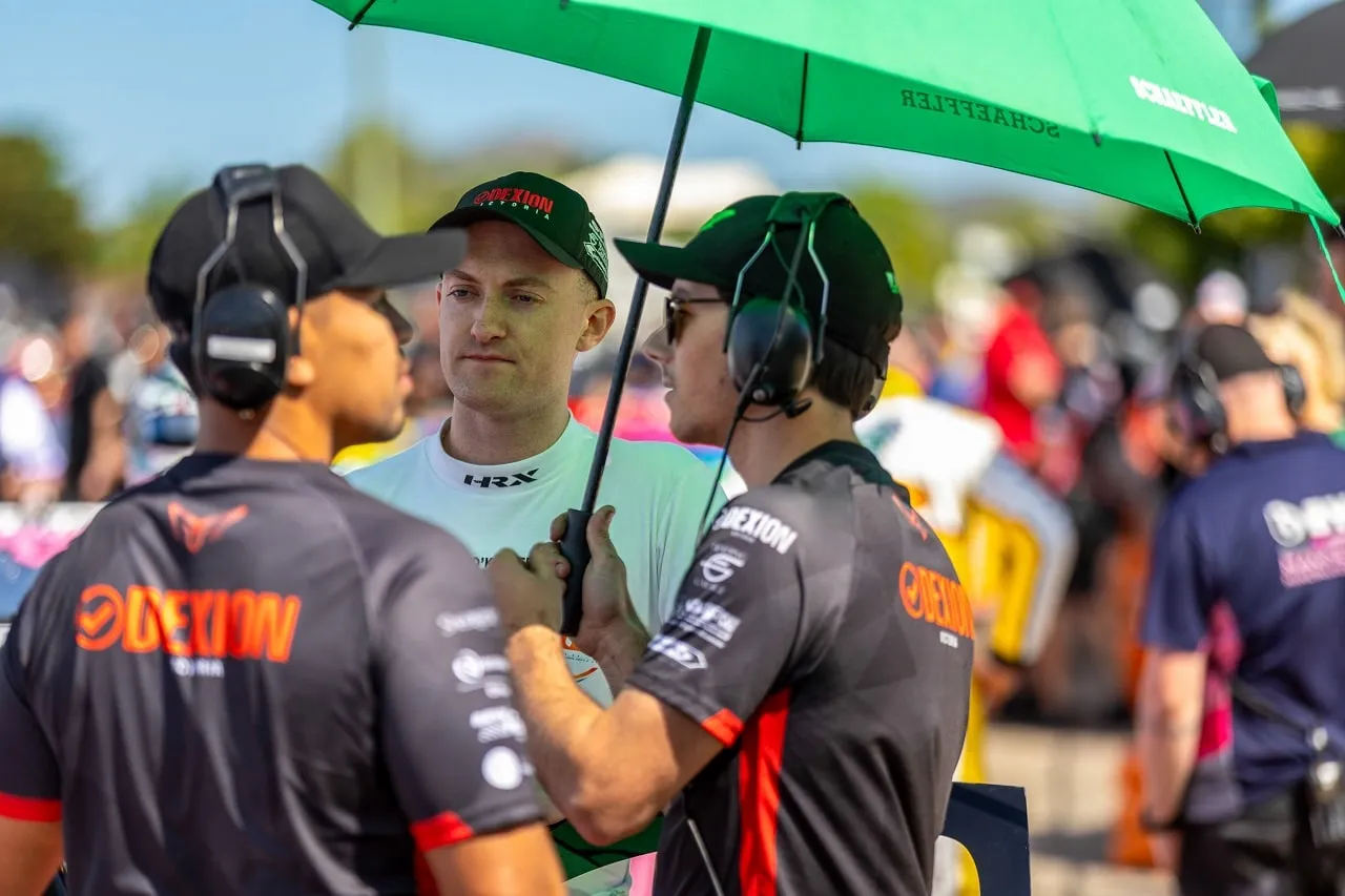 Team members in Dexion shirts and headsets speaking with a driver under a green Schaeffler umbrella on the grid