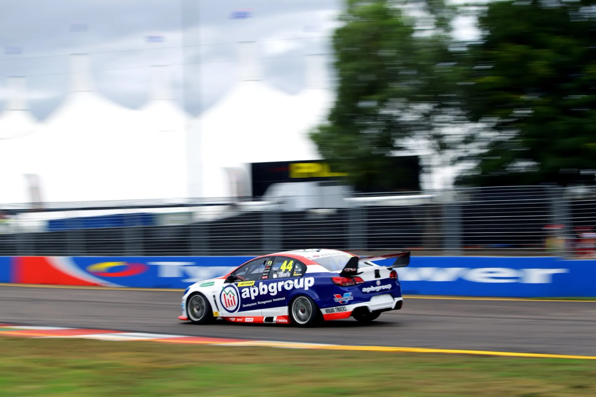 Rear side view of the #44 apbgroup Commodore Supercar at speed beside a blurred trackside fence