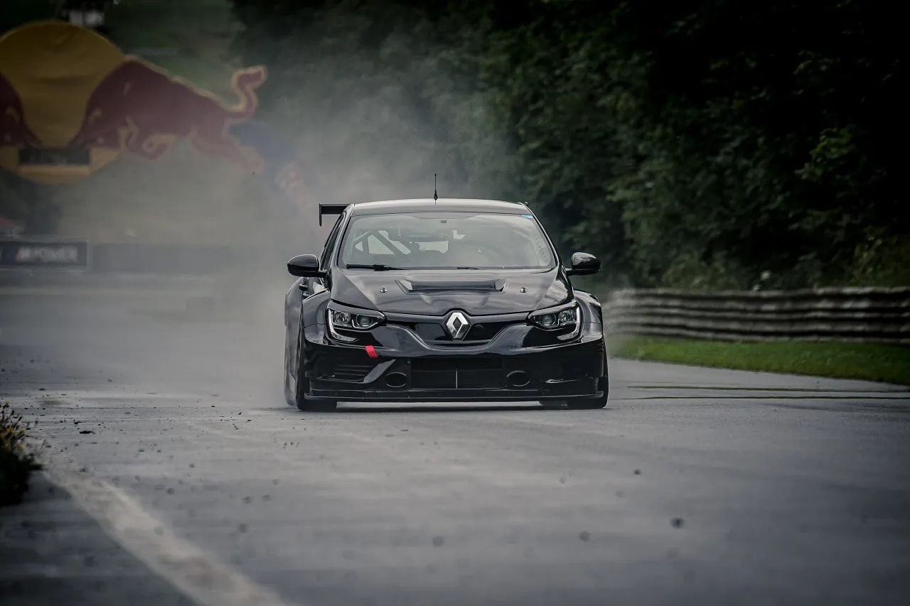 The black Renault Megane TCR car driving through a cloud of spray on a damp track with trees behind