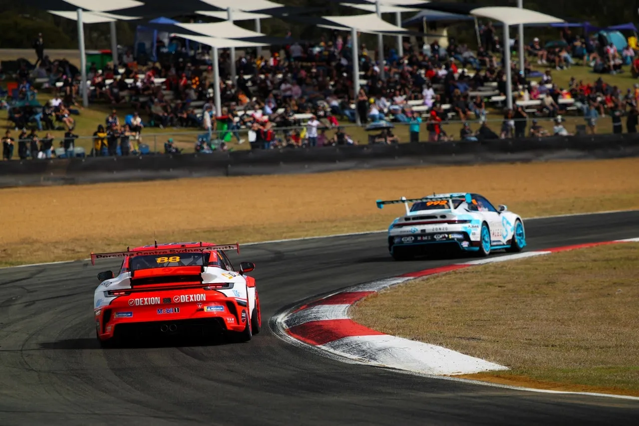 Rear view of the Dexion Porsche #88 and a light blue Porsche on track in front of a grandstand