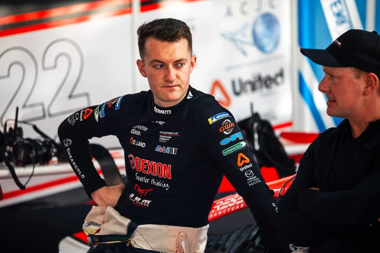 Dylan O’Keeffe in a Dexion race suit looking to one side, with a team member beside him