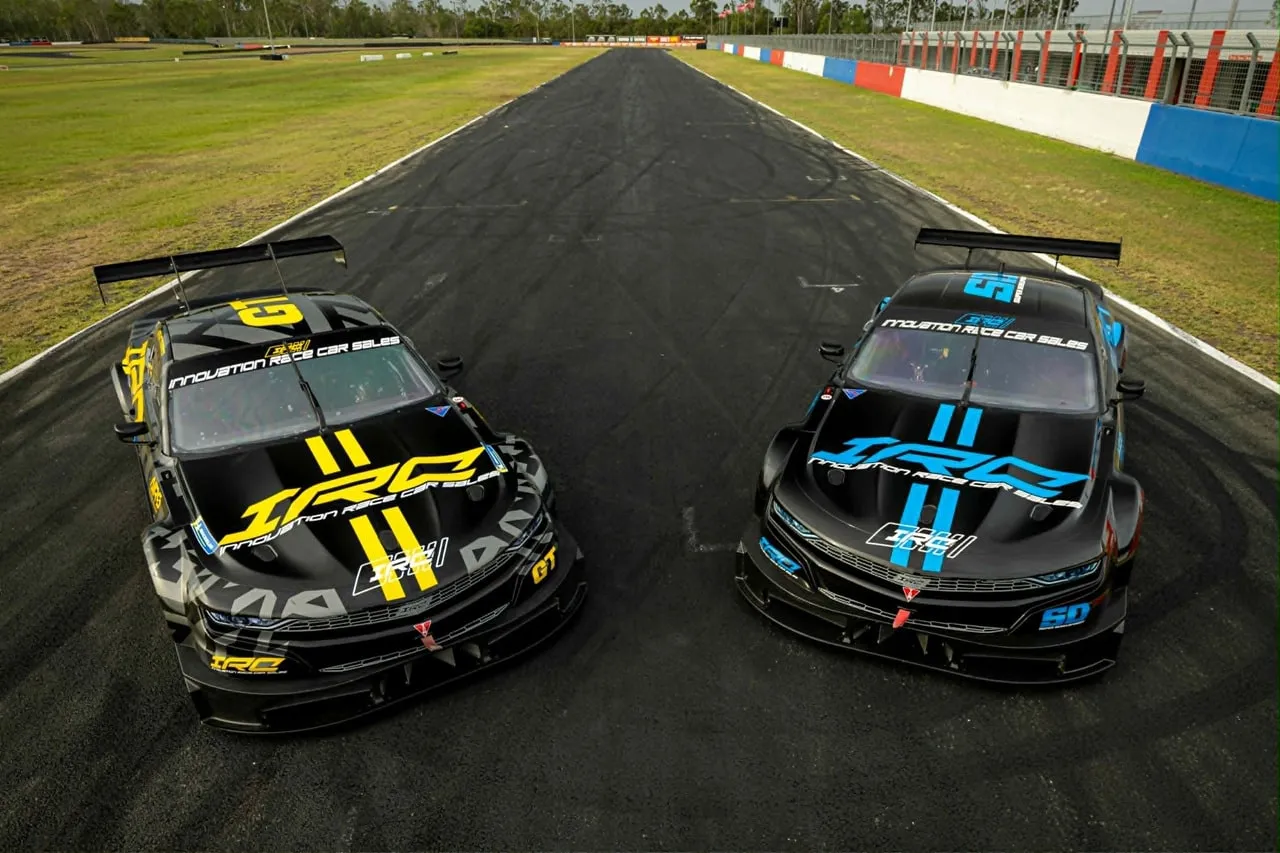 Two black IRC race cars, one with yellow graphics and one with blue, parked side by side on a circuit