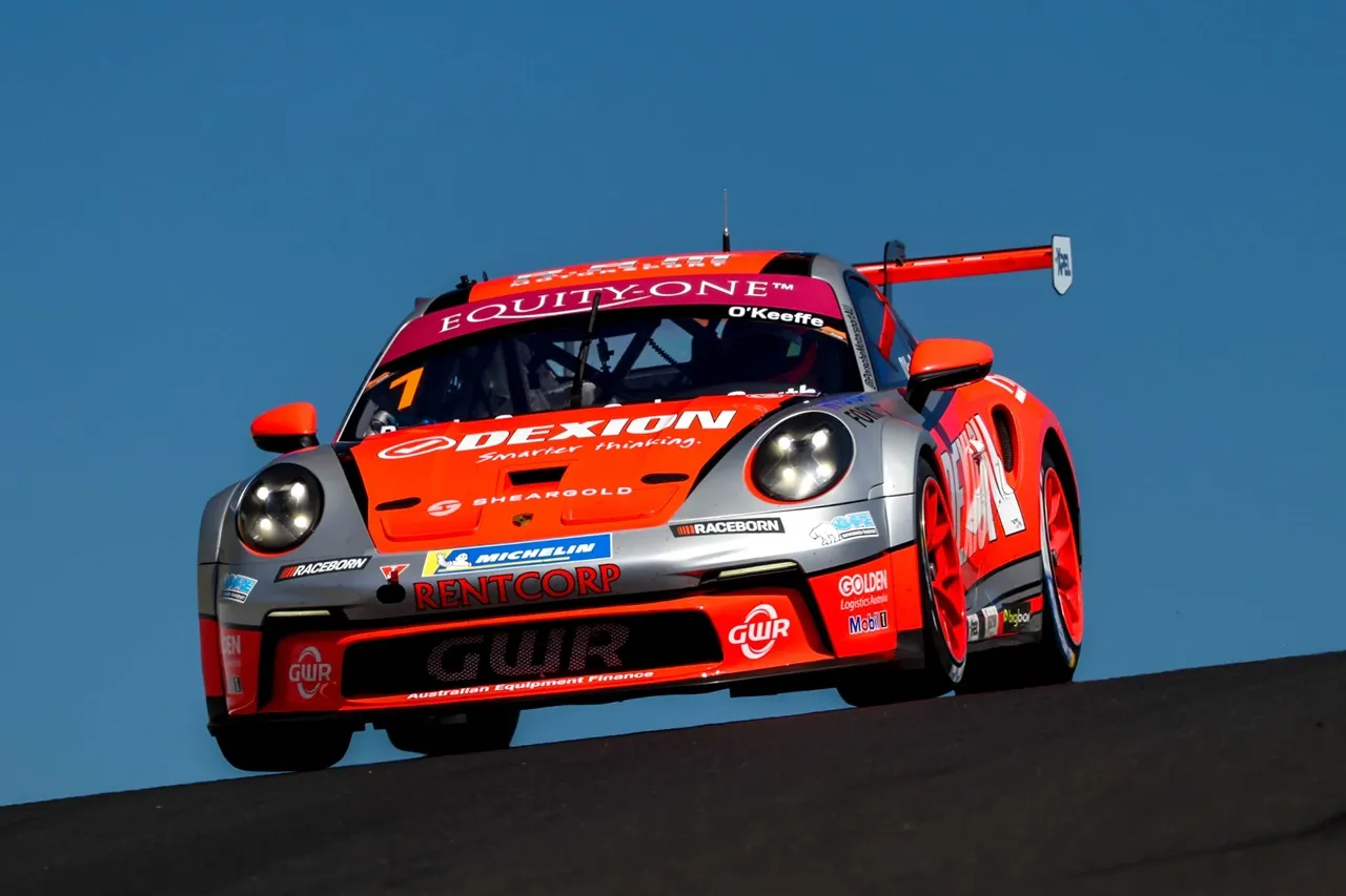 The #1 Dexion Porsche cresting a rise head-on against a clear blue sky at Mount Panorama