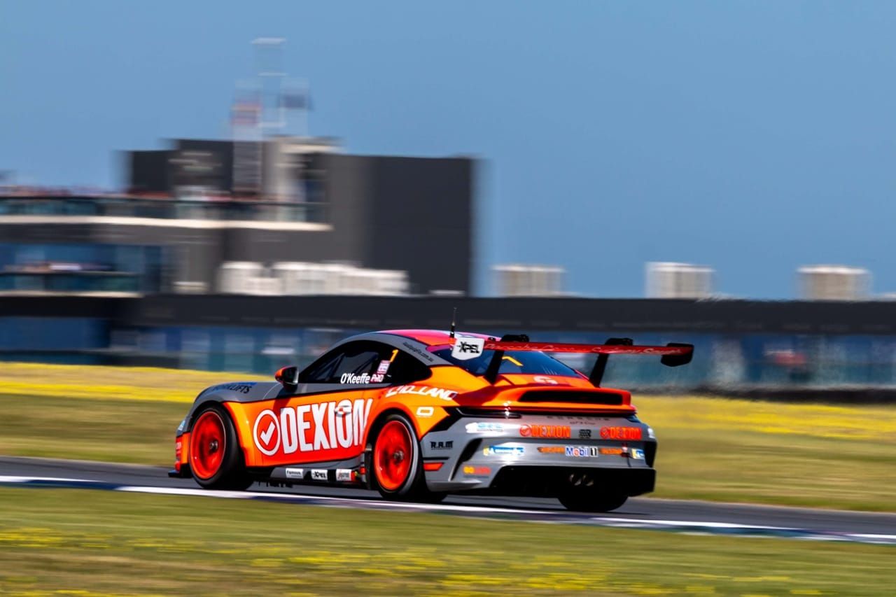 Dylan O’Keeffe’s orange and silver Dexion Porsche at speed at The Bend, grandstand behind