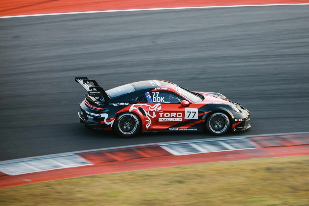 Black and red Toro Racing Porsche 911 GT3 Cup car #77 with DOK on the window, on track