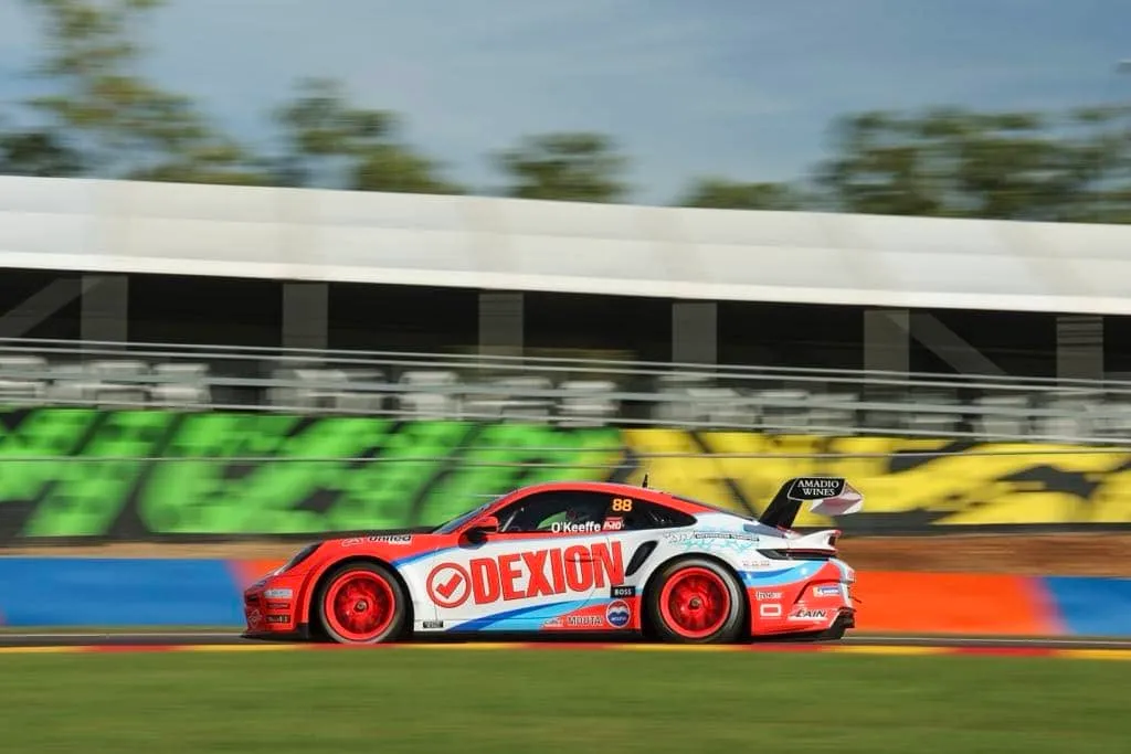 Side view of the number 88 Dexion Porsche 911 GT3 Cup car at speed in front of a grandstand and graffiti wall