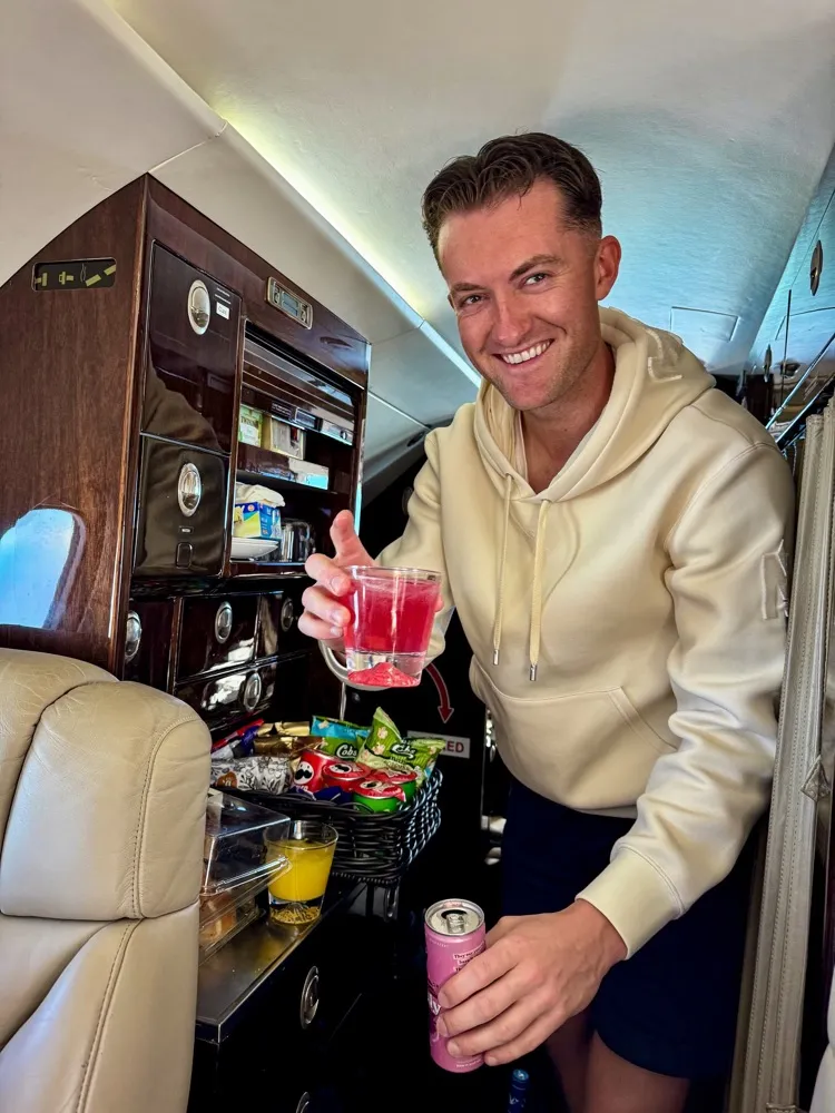 A smiling man in a cream hoodie holding a drink