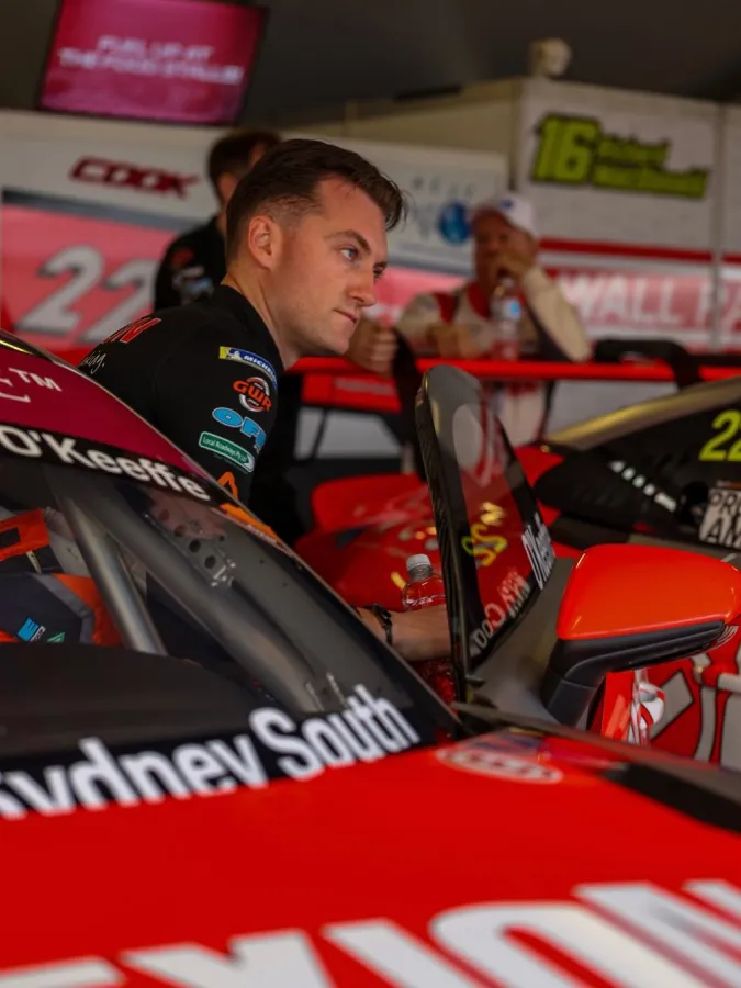 A driver in team gear leaning over the cockpit of the red Dexion Porsche in the garage
