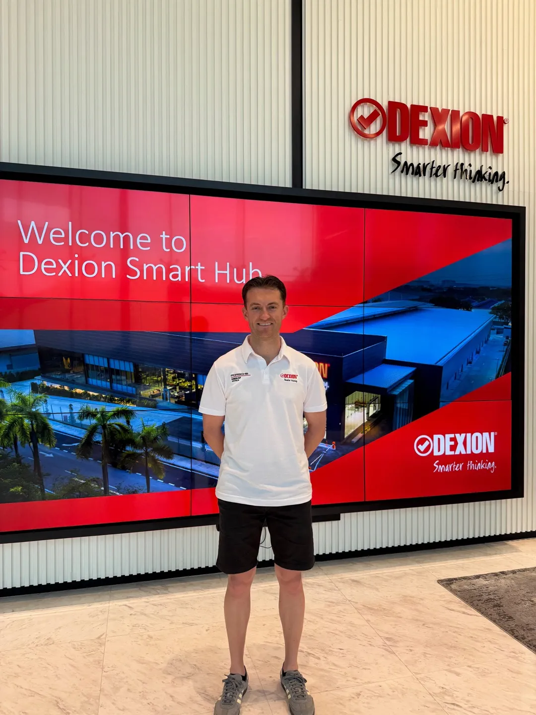 A man in a Porsche Carrera Cup polo standing in front of a “Welcome to Dexion Smart Hub” screen