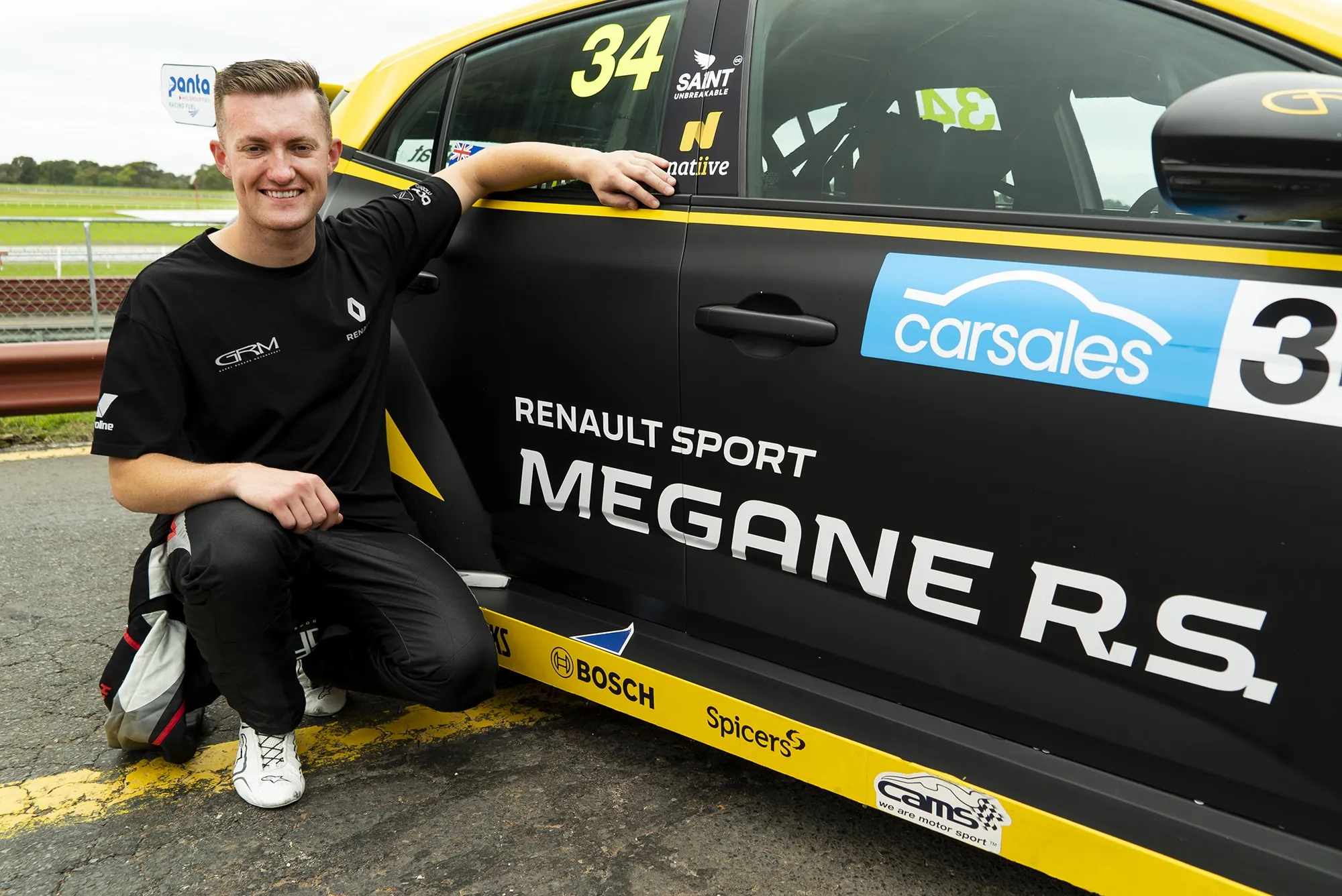 Dylan O’Keeffe crouching and smiling beside the yellow Renault Megane R.S. TCR car in a black GRM shirt